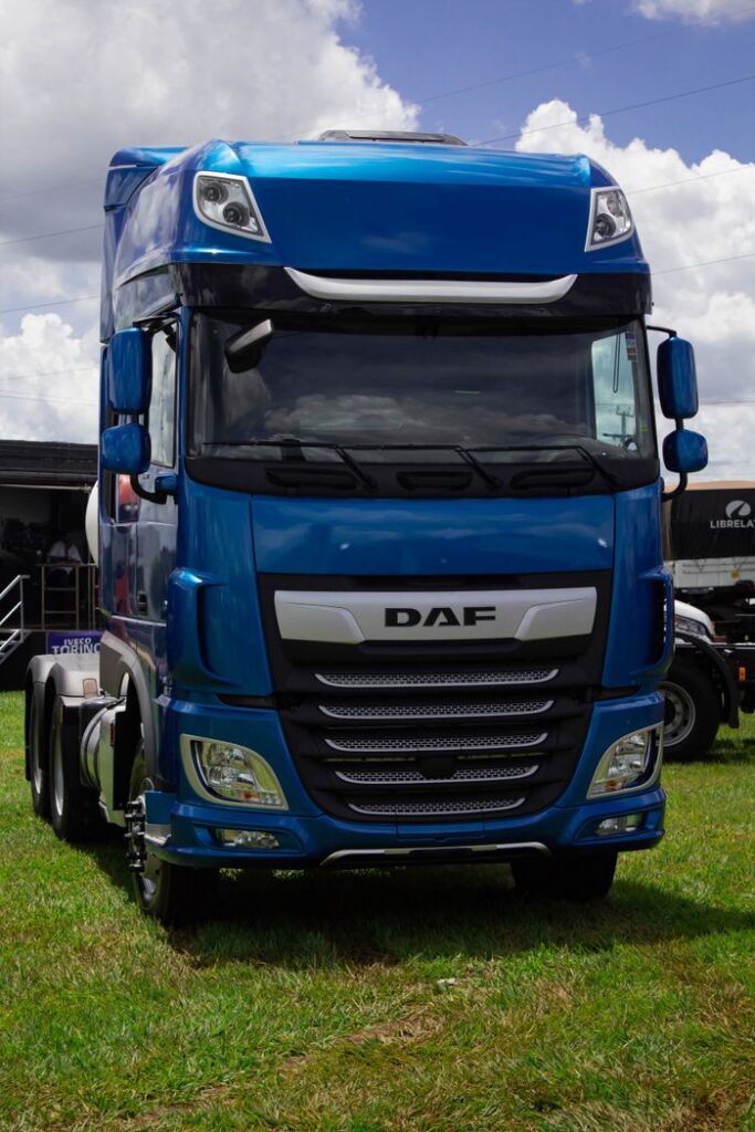 Front view of a blue DAF truck parked on a grassy area with a cloudy sky overhead.